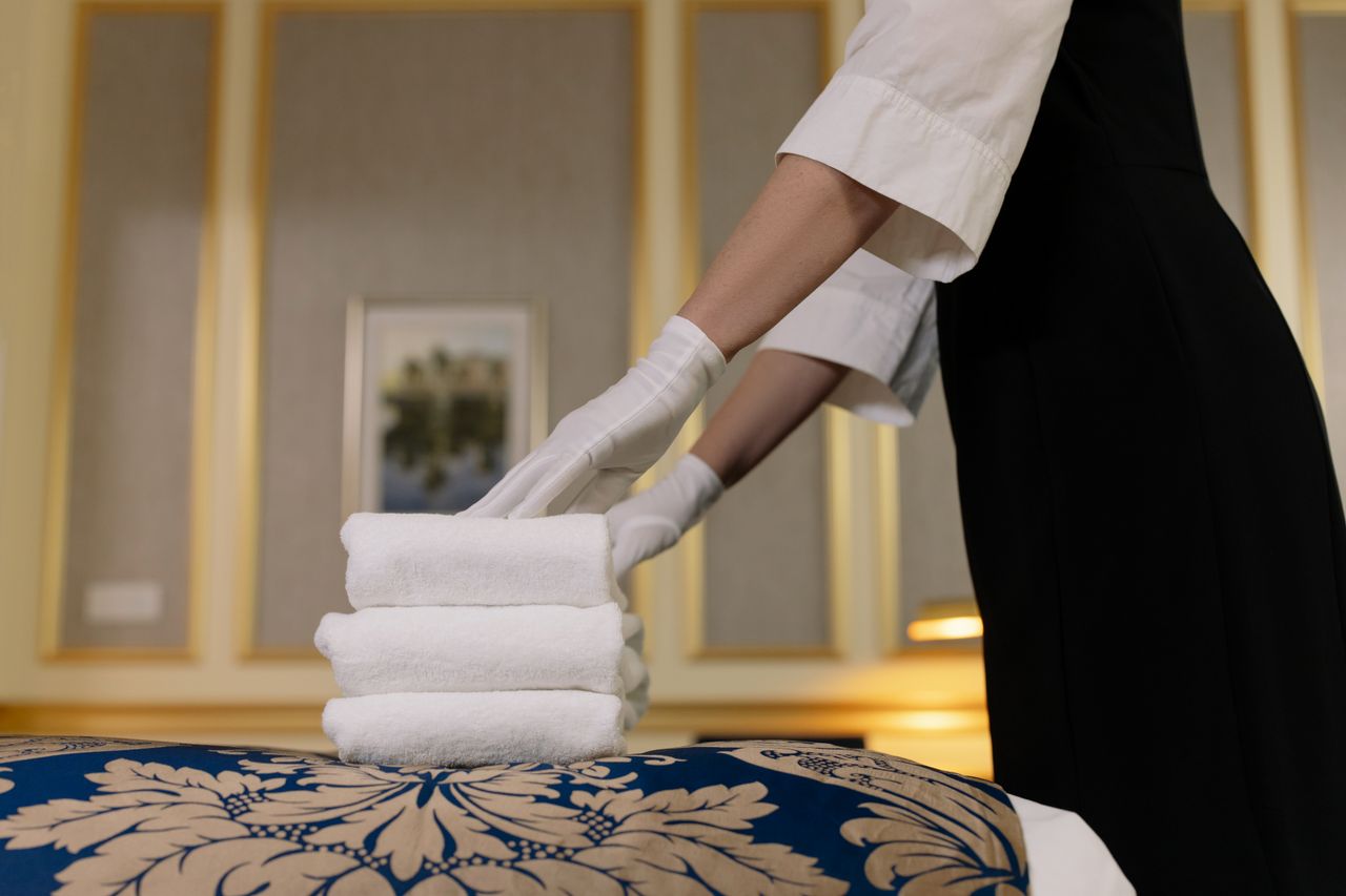 In a luxurious room, a hotel housekeeper carefully arranges clean towels in a tidy stack.